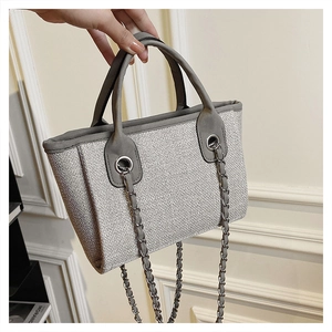 Detail of grey woven bucket bag featuring silver chain strap and leather trim handles