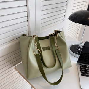 Detail of light green PU leather tote bag with olive straps and metal chain on a desk