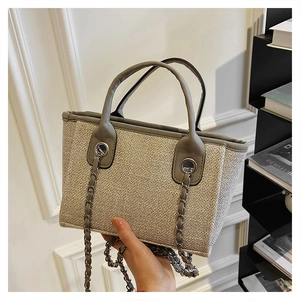 Detail of woven straw bucket bag with gray leather trim and silver metal chain strap