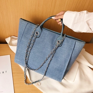 Denim blue woven tote bag with chain strap and large capacity on wooden table