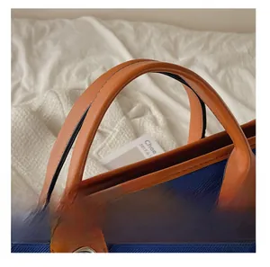 Detail of blue canvas bag with brown leather handles and silver ring metal hardware