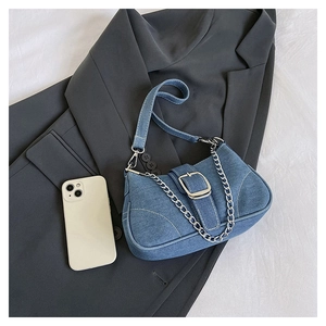 Detail of blue denim shoulder bag with silver chain, white stitching, and silver buckle