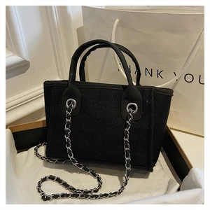 Detail of a black canvas bucket bag with silver metal eyelets and a chain strap