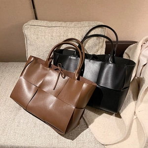 Grands sacs cabas en cuir tressé marron et noir avec nœuds sur un canapé beige