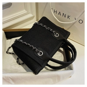 Detail of black canvas bucket bag with silver chain strap and top handles in a box