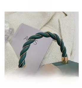 Close-up of dark green crossbody bag with woven twisted handle and gold metal clasp hardware
