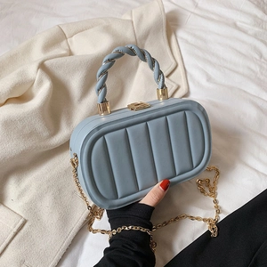 Light blue padded crossbody bag with twist handle and gold chain strap in a lifestyle setting