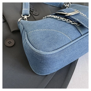 Close-up of blue denim handbag with silver chain and metal buckle detail