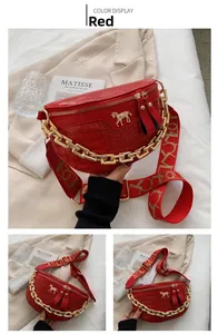 Detail of red crocodile textured chest bag with thick gold chain and wide logo strap