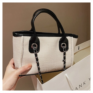 Detail of contrast canvas bucket bag with black leather trim and metal chain strap