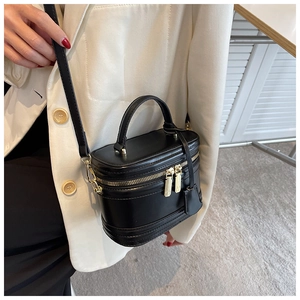 Close-up of black box crossbody bag with gold zippers and top handle on a white suit