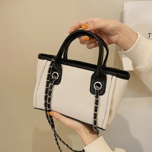 Minimalist canvas tote bag with black leather trim and silver chain strap for women