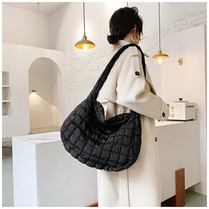Close-up of the quilted texture on a large black puffer tote bag worn by a model