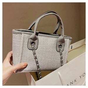 Detail of gray woven tote bag with silver chain and leather handle inside a shopping bag
