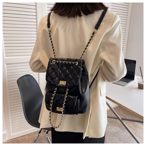 Detail of black quilted leather backpack with gold chain straps and twist locks on model