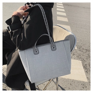 Macro shot of grey tweed tote bag with silver chain strap and leather handle in outdoor setting