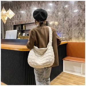 Detailed back view of a white quilted puffer tote bag worn by a model in a cozy cafe