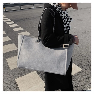 Detailed view of grey woven tote bag with chain strap styled with black coat and scarf