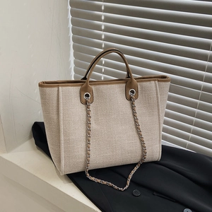 Minimalist beige canvas tote bag with brown leather trim and metal chain detail on window ledge