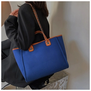 Detail of royal blue tote bag with orange trim and chain strap shown on a model