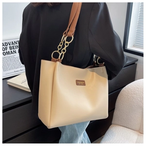 Detail of cream tote bag with brown straps and golden chain accents on a model shoulder
