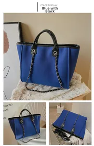 Detail view of blue canvas tote bag with black leather trim and metal chain strap