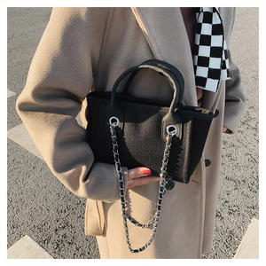 Detail of black woven bucket bag with silver chain and twin handles on a camel coat