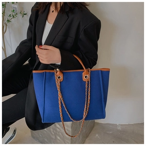 Blue felt tote bag with brown leather trim and metal chain strap shown on a model