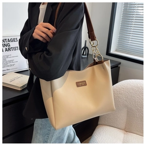 Detail of beige tote bag with dark brown straps and golden chain hardware on model