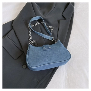 Detail of blue denim baguette bag with silver metal chain and wide fabric strap