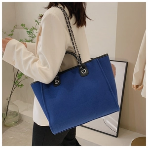 Detail of royal blue tote bag with black leather handles and metal chain strap in use