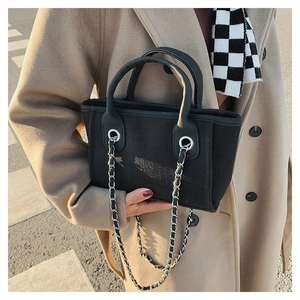 Detail of black woven bucket bag with silver chain strap and leather reinforcements