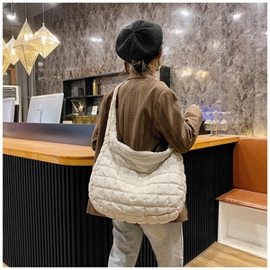 Detailed view of a white quilted down tote bag with a soft puffy texture on a female model