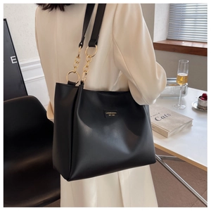 Close-up of black leather tote bag featuring gold logo emblem and chain strap details