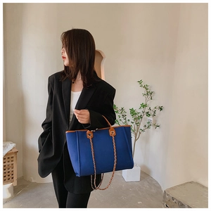 Detail of navy canvas tote bag with brown leather trim and metal chain shoulder strap