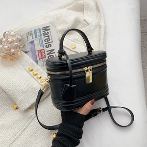 Minimalist black cylinder shoulder bag with gold zipper and top handle on tweed fabric
