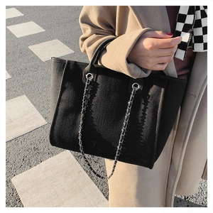 Detail of black canvas bucket bag featuring a double chain strap and leather handle