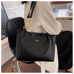 Detail of black leather tote bag featuring gold chain strap and brand logo plaque