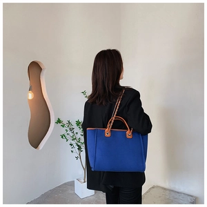 Blue canvas tote bag with leather trim worn by model in a minimalist modern interior
