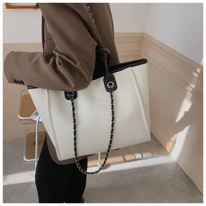 Model wearing a large cream tote bag with black contrast trim and chain shoulder strap