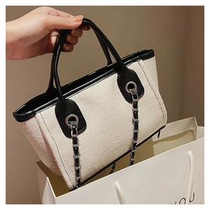 Detail of beige textured fabric tote with black leather trim and silver chain handles