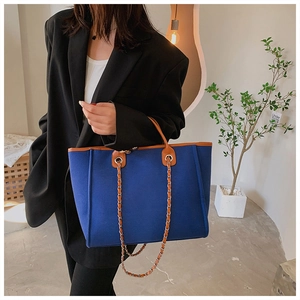 Close-up of blue canvas tote bag with brown leather trim and metallic chain strap detail