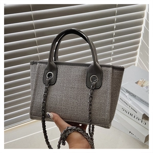 Detailed macro view of gray woven tote bag featuring chain strap and leather handle
