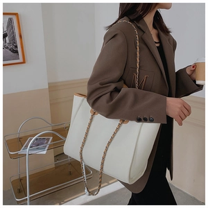 Close-up of white tote bag with woven metal chain strap on woman in brown blazer