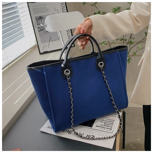Detail of navy blue felt tote bag with black leather handles and silver chain strap