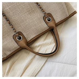 Detail of woven tote bag with brown leather handle and silver metal chain strap