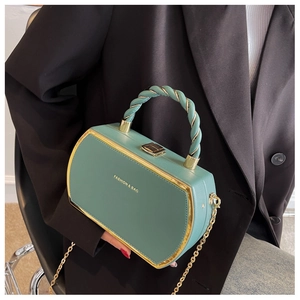Detail of green leather box bag with gold metal frame and woven handle shown on model