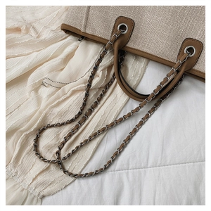 Close-up of woven straw tote bag with brown faux leather trim and chain shoulder strap