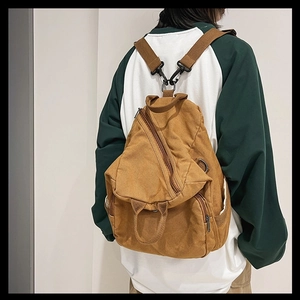Detail view of brown canvas backpack with unique triangular zipper and metal hooks