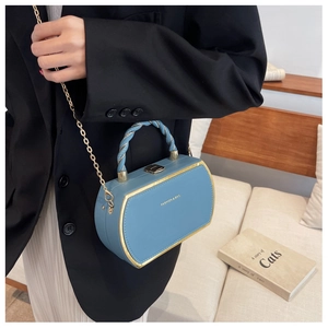 Detail of sky blue box bag with gold metal corners and spiral handle on a black blazer